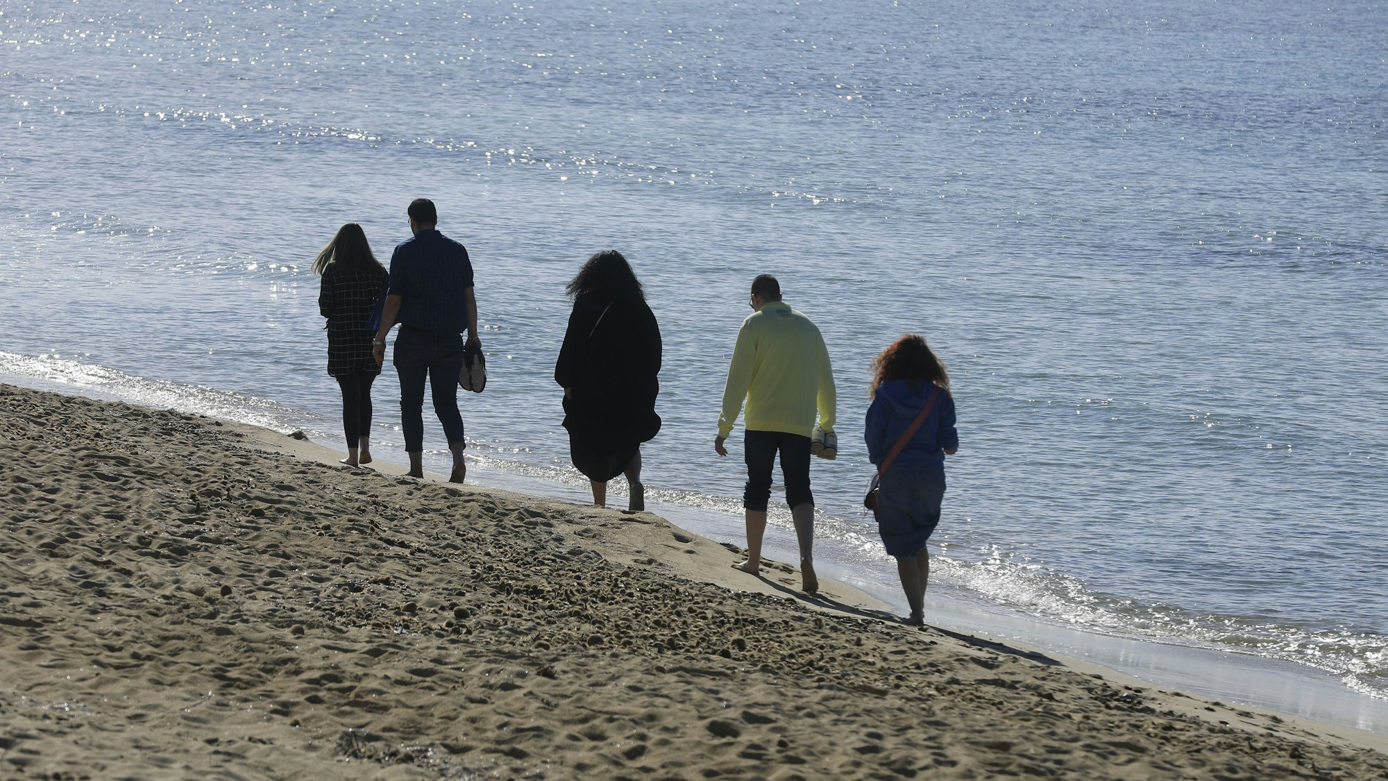 Menschen spazieren bei sonnigem Wetter am Strand von Arenal entlang.