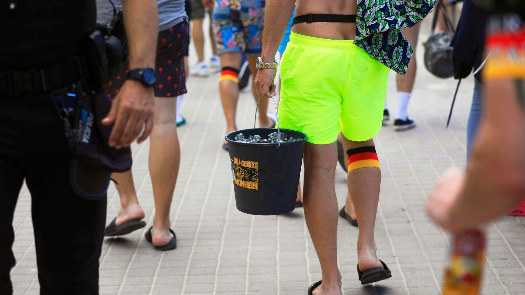 Spanien-Touristen tragen einen Eimer mit dem BVB-Logo mit Flaschen, als sie an der Promenade am Strand Arenal entlang spazieren.