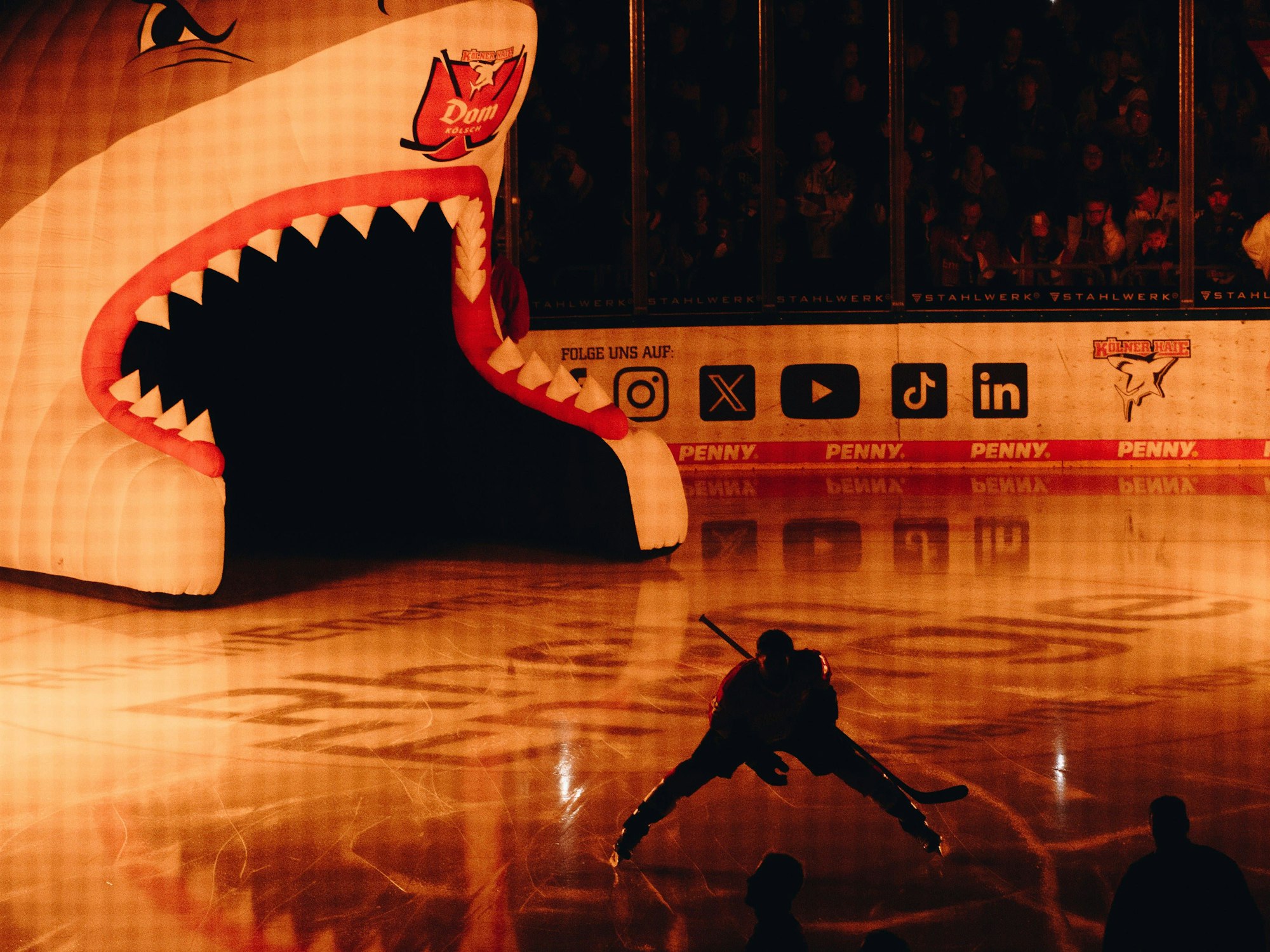Ein Profi der Kölner Haie kommt aus einem großen, aufblasbaren Hai-Maul aufs Eis gefahren.