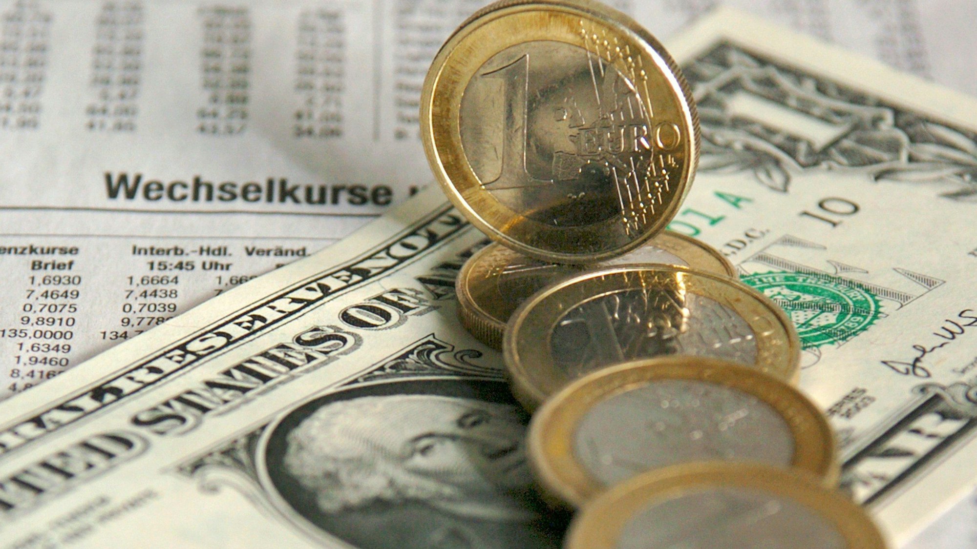 Ein-Euro-Münzen liegen über einer Dollarnote verteilt über den Wechselkursen für Devisen in der Tageszeitung (Symbolbild vom 5. Januar .2004).