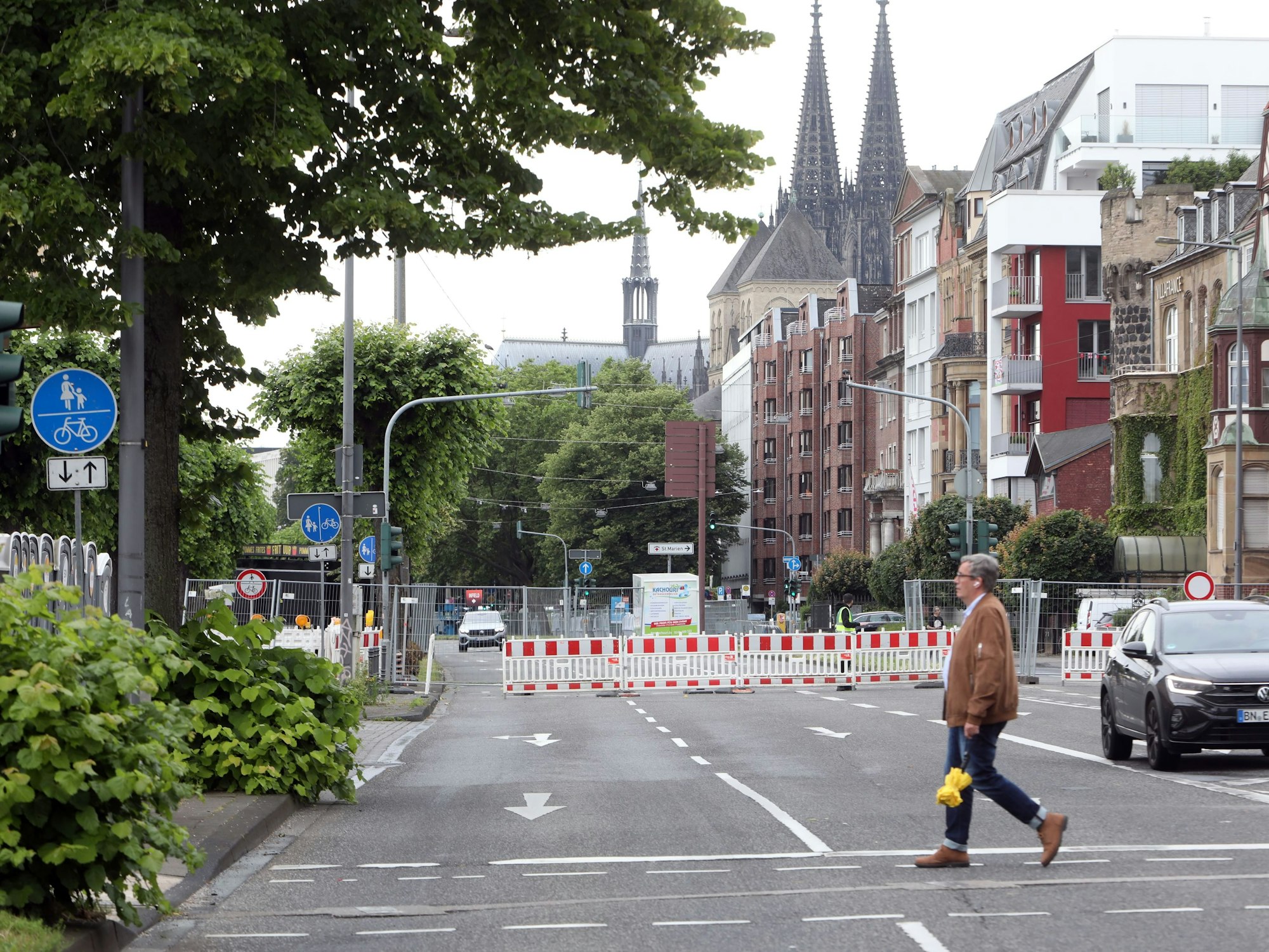 Geht über eine Straße am Kölner Rheinufer, im Hintergrund sind Autos und Absperrungen zu sehen.