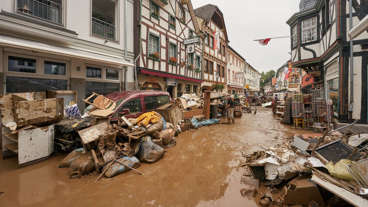 Eine Straße steht voller Wasser, vor den Häusern stapeln sich kaputte Möbel.