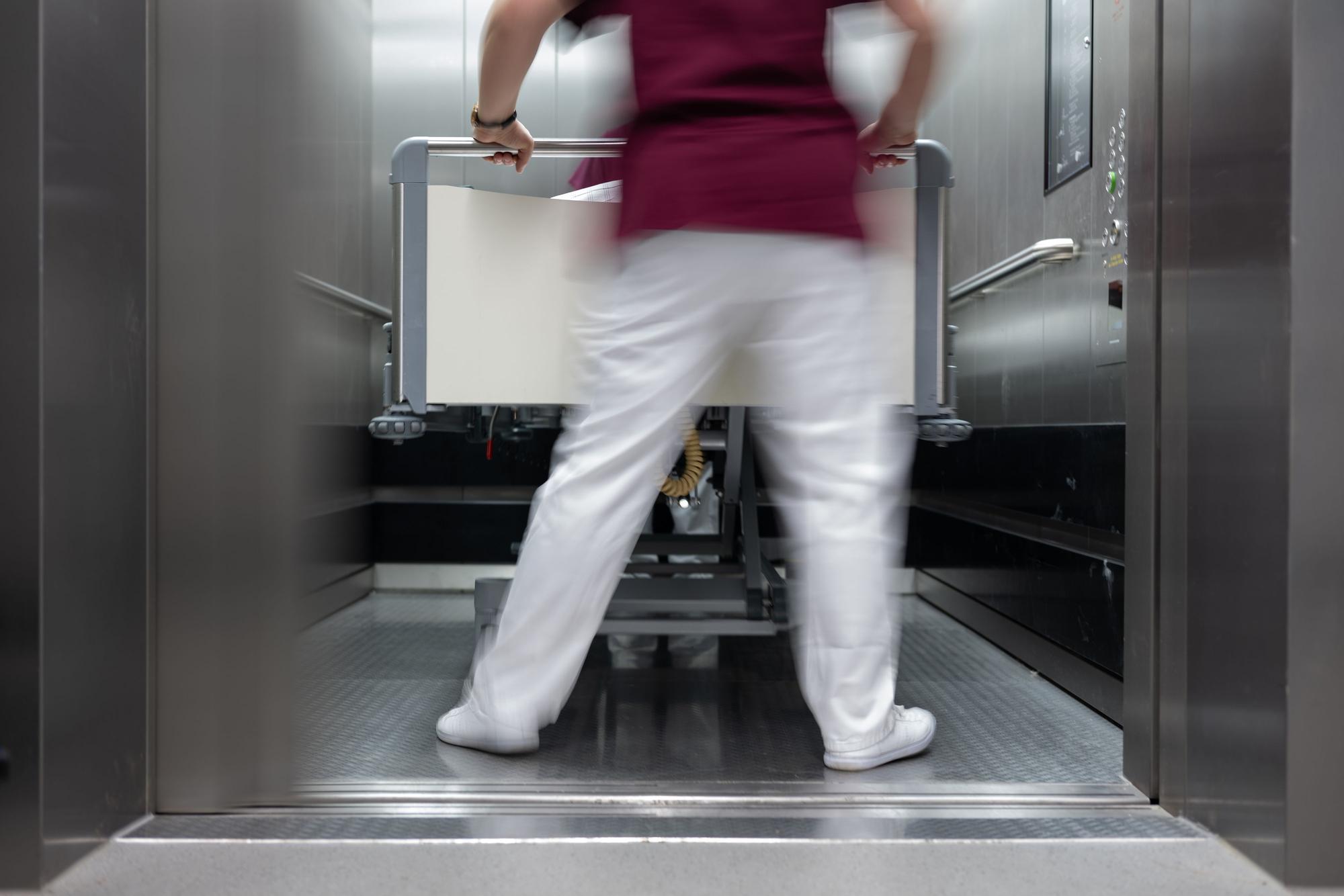 Eine Krankenpflegerin und ein Krankenpfleger schieben ein Krankenbett aus einenm Aufzug eines Krankenhauses.