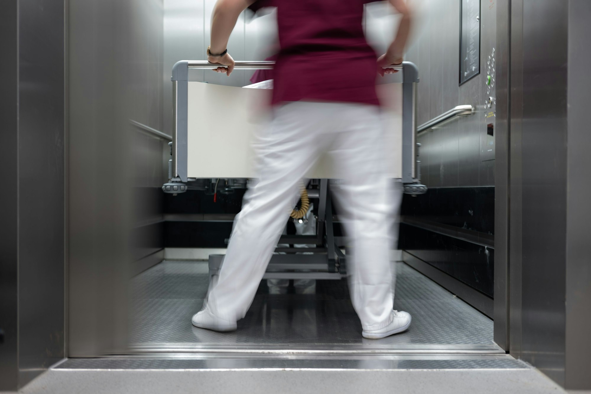 Eine Krankenpflegerin und ein Krankenpfleger schieben ein Krankenbett aus einenm Aufzug eines Krankenhauses.