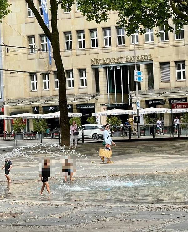 Kinder spielen im neuen Brunnen am Neumarkt in Köln, auch eine erwachsene Frau ist im Wasser.