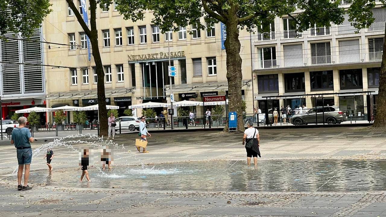 Kinder spielen im neuen Brunnen am Neumarkt in Köln, auch eine erwachsene Frau ist im Wasser.