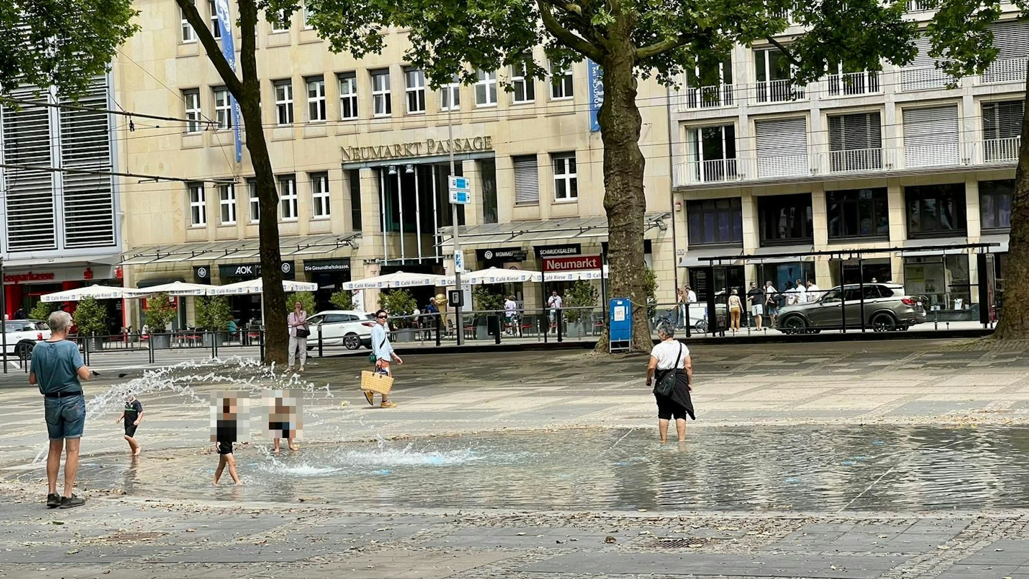 Kinder spielen im neuen Brunnen am Neumarkt in Köln, auch eine erwachsene Frau ist im Wasser.