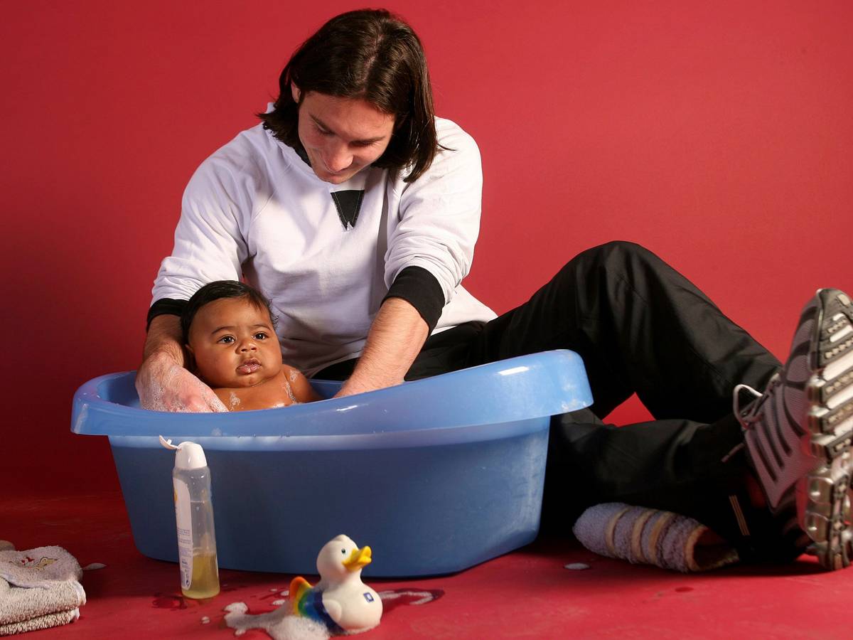 Lionel Messi badet ein Baby in einer Plastikwanne.