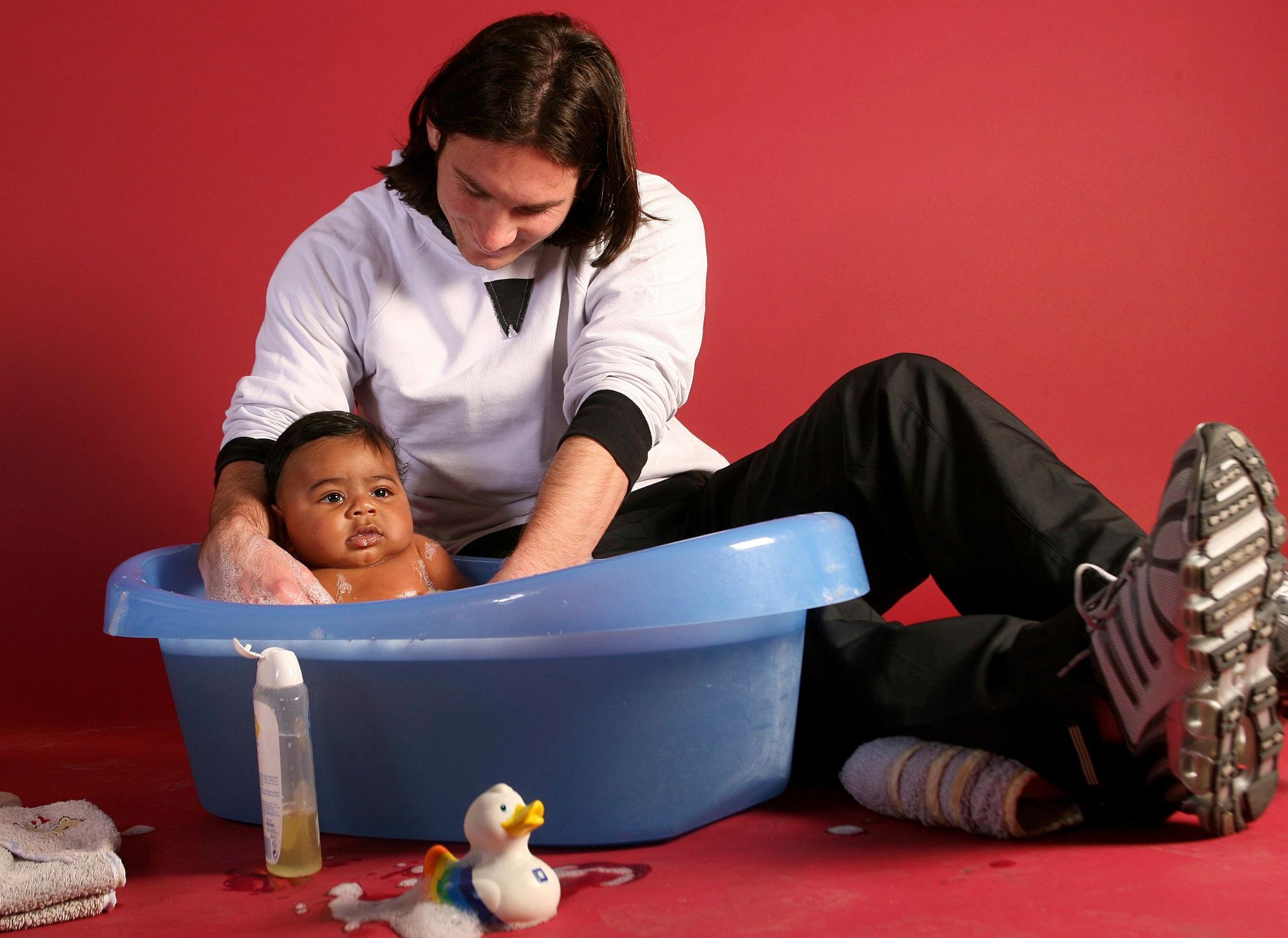 Lionel Messi badet ein Baby in einer Plastikwanne.