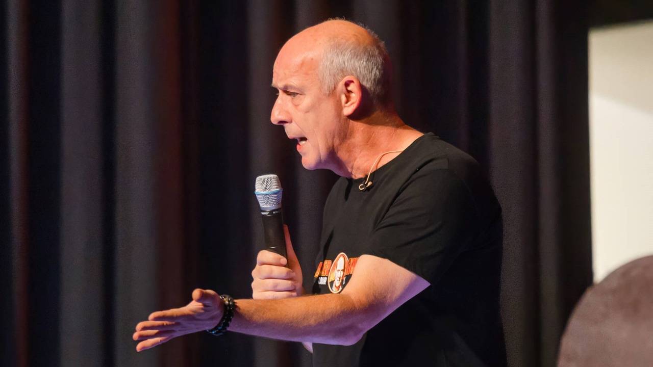 Mario Basler mit Mikrofon in der Hand bei einem Bühnen-Auftritt.