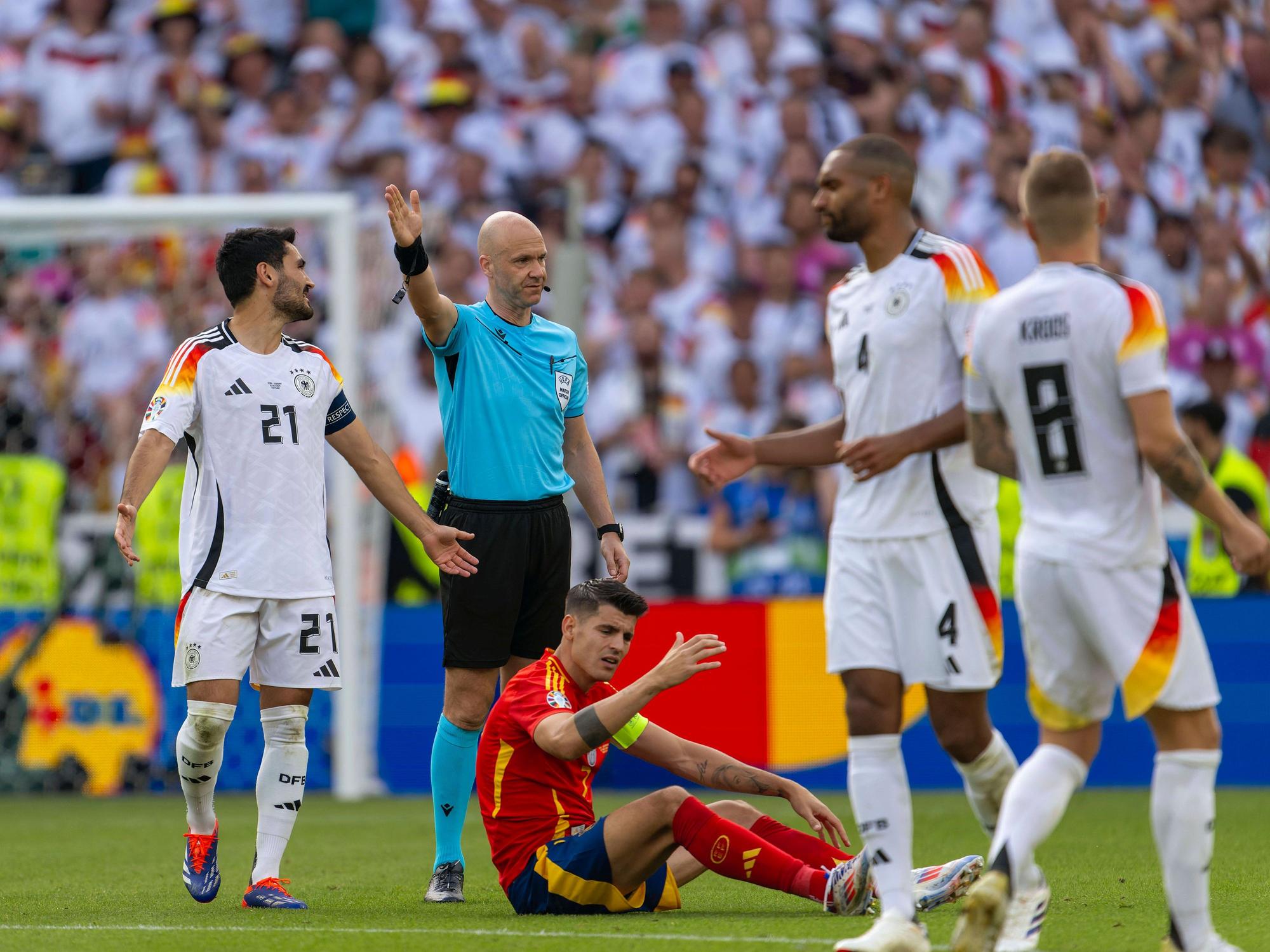 Schiedsrichter Anthony Taylor beim EM-Viertelfinale zwischen Spanien und England, um ihn herum beschweren sich die beiden Kapitäne Ilkay Gündogan (l.) und Álvaro Morata.