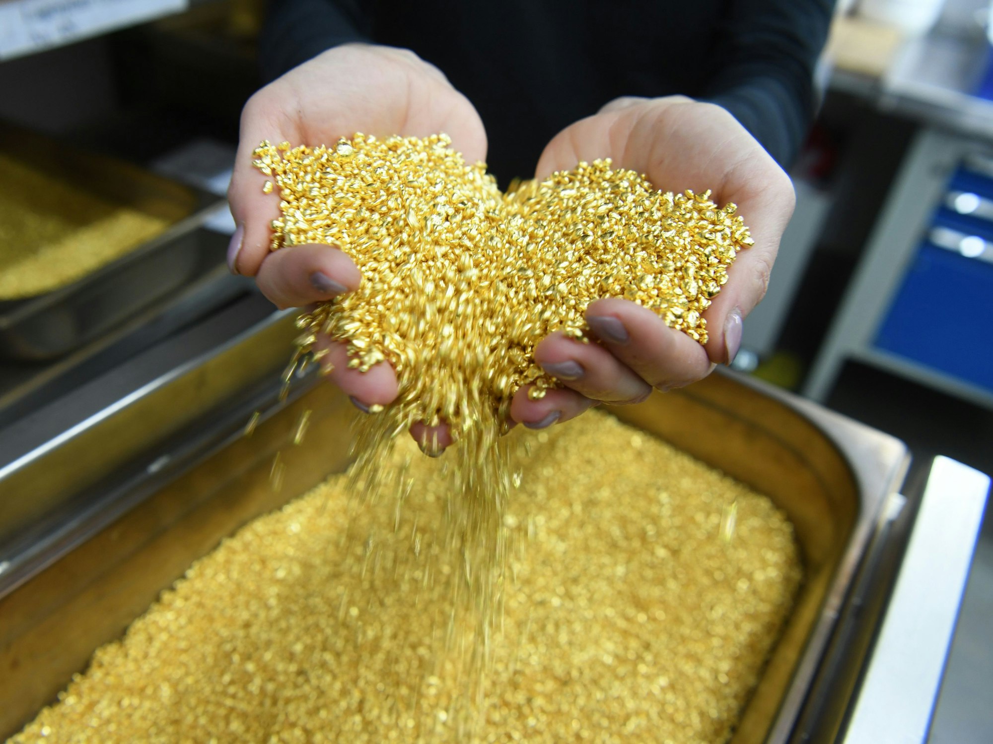 Goldgranulat rieselt durch zwei Hände.