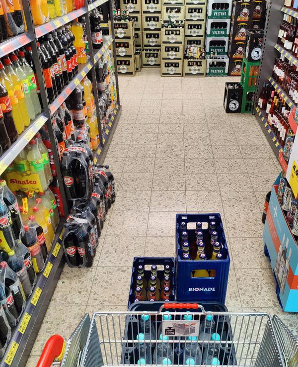 Einkaufswagen wird durch einen Gang im Getränkemarkt geschoben.