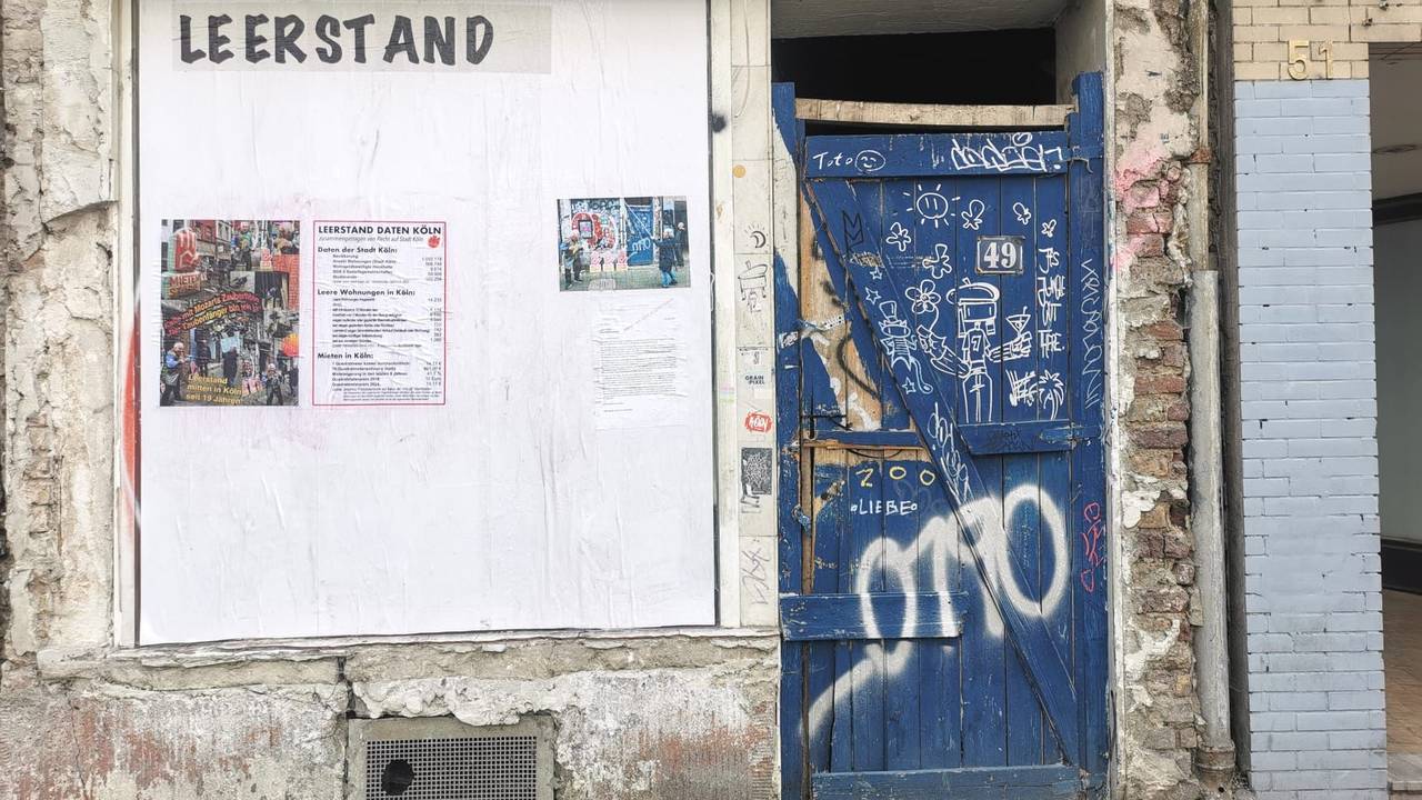 Blick auf einen Hauseingang mit einem Plakat an der Fassade.