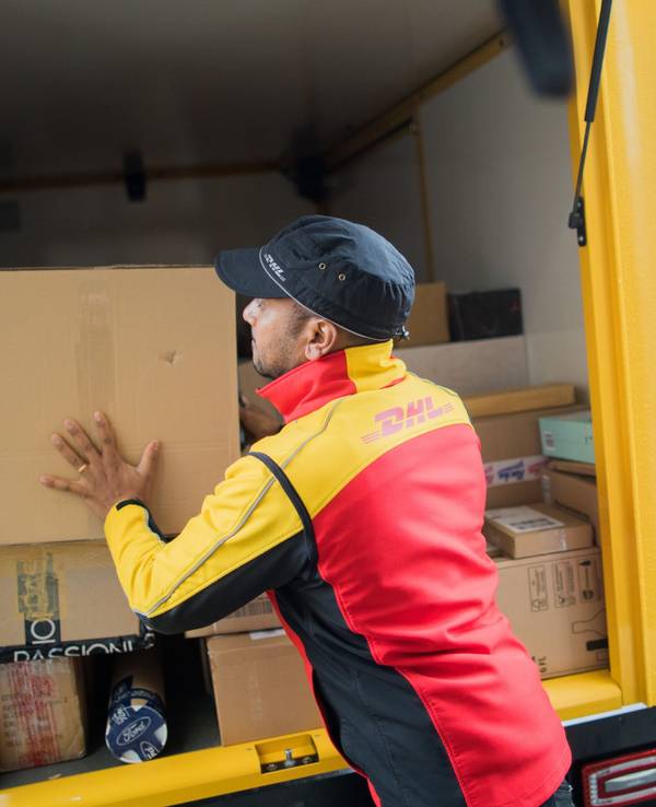 Ein Paketzusteller stellt ein Paket in ein Fahrzeug der Deutschen Post DHL.