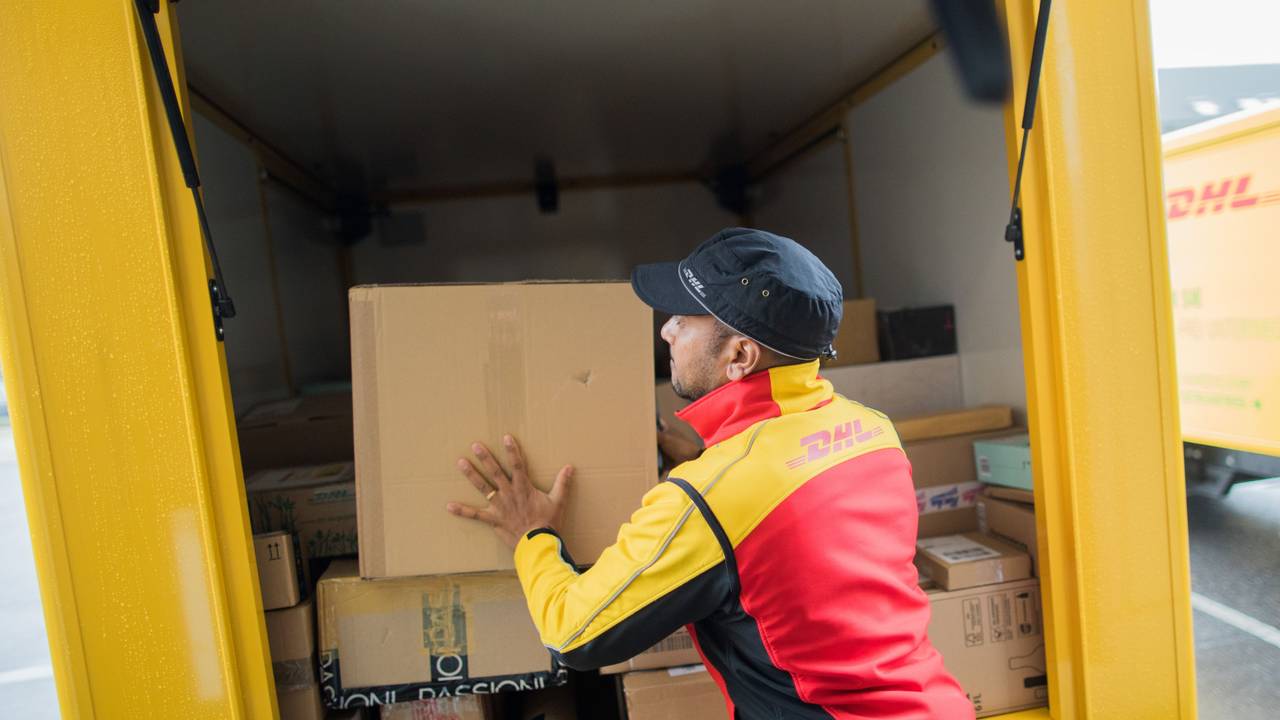 Ein Paketzusteller stellt ein Paket in ein Fahrzeug der Deutschen Post DHL.
