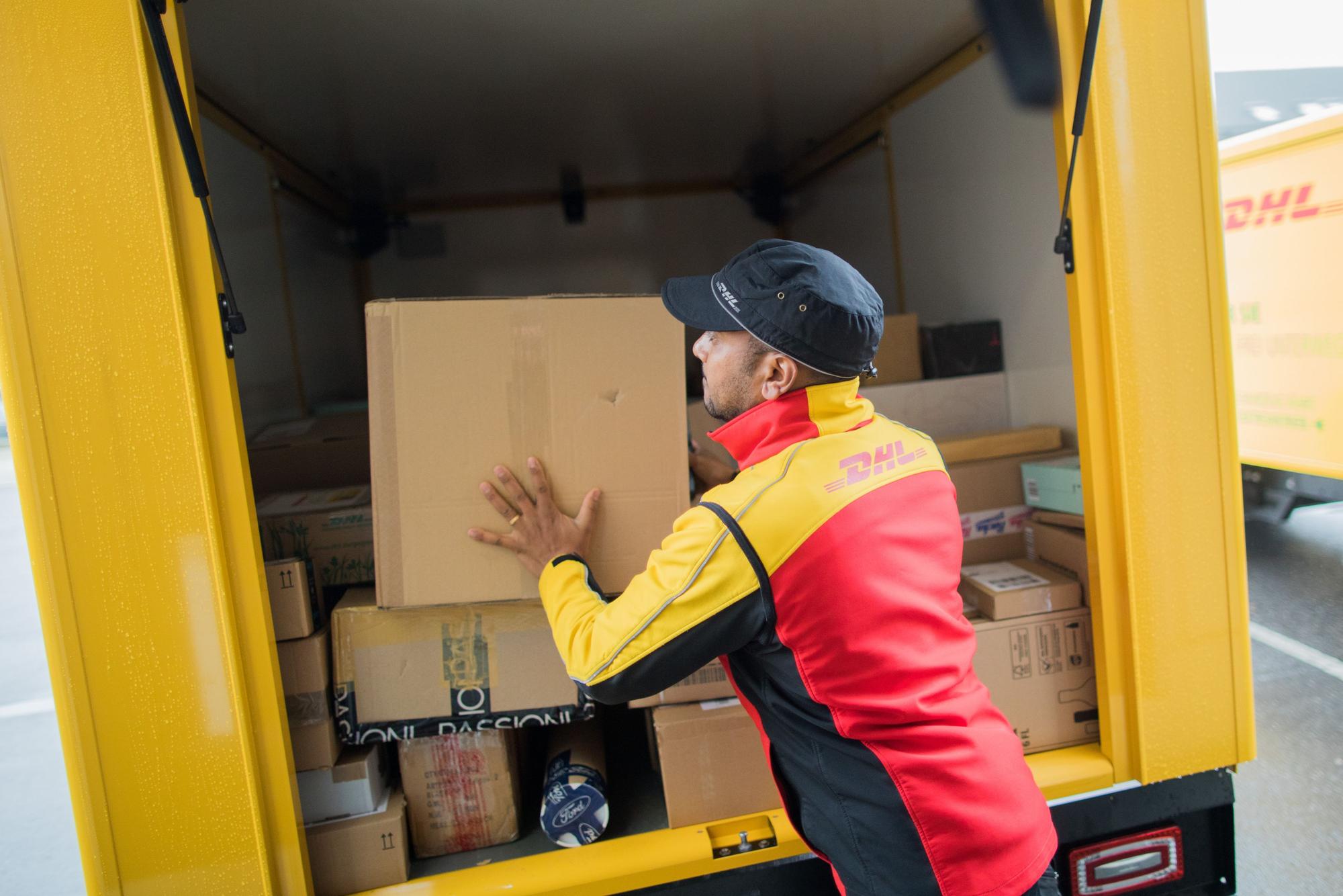 Ein Paketzusteller stellt ein Paket in ein Fahrzeug der Deutschen Post DHL.