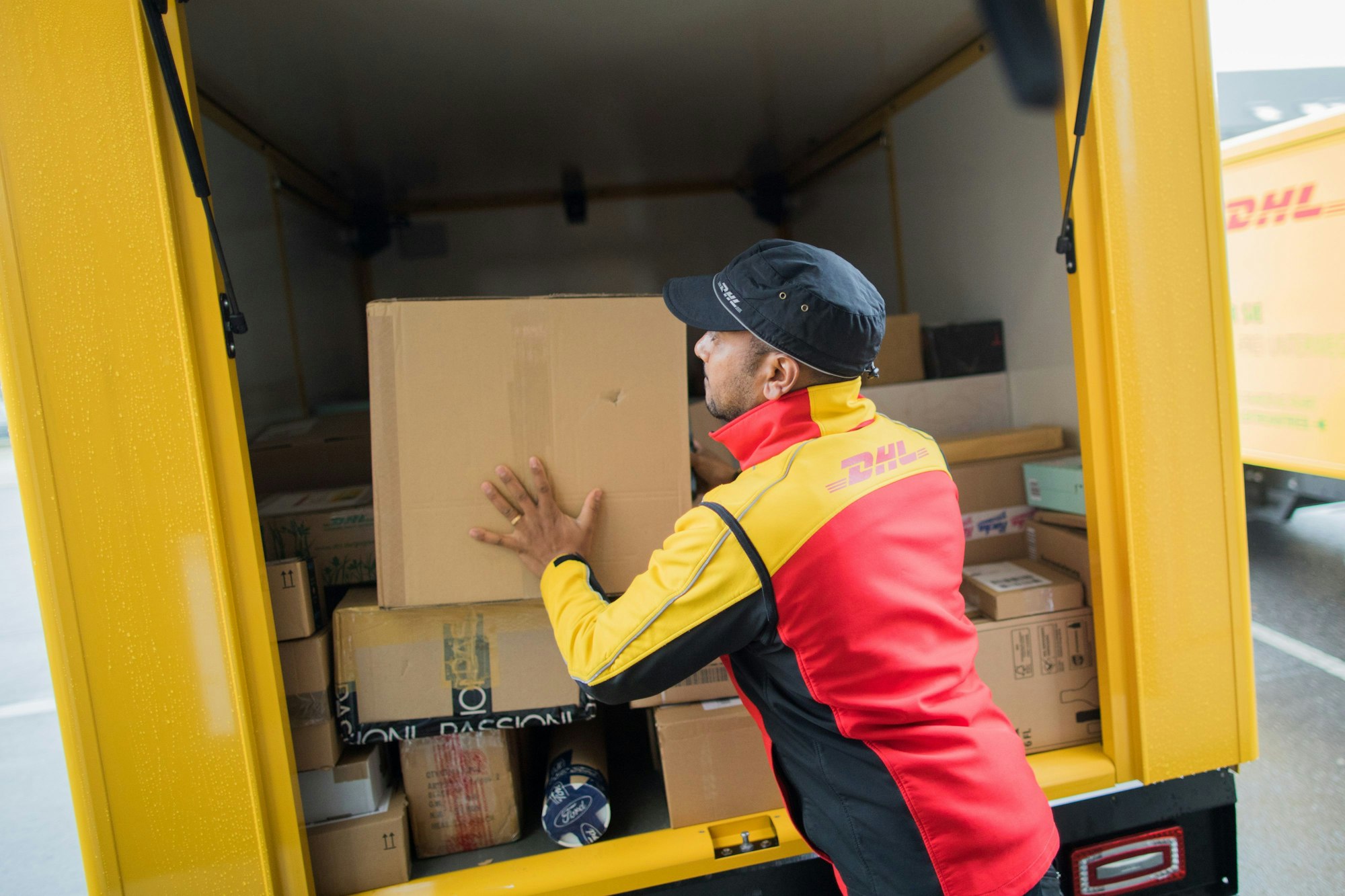 Ein Paketzusteller stellt ein Paket in ein Fahrzeug der Deutschen Post DHL.