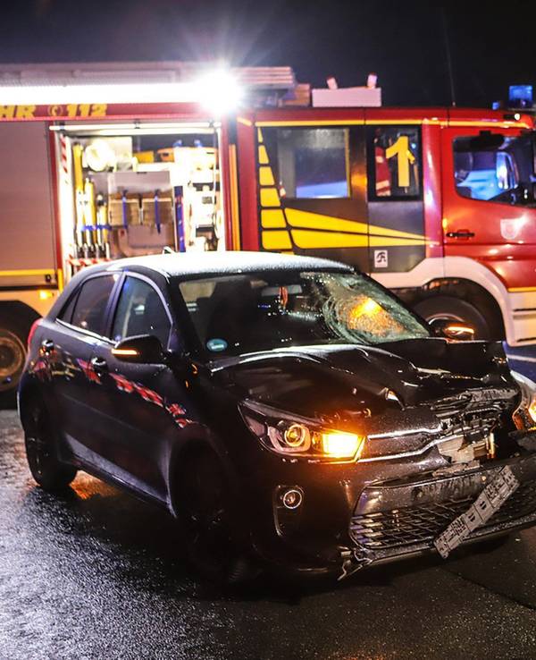 Einsatzkräfte der Feuerwehr stehen neben einem stark beschädigten Auto.