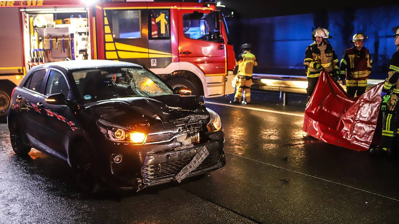 Einsatzkräfte der Feuerwehr stehen neben einem stark beschädigten Auto.