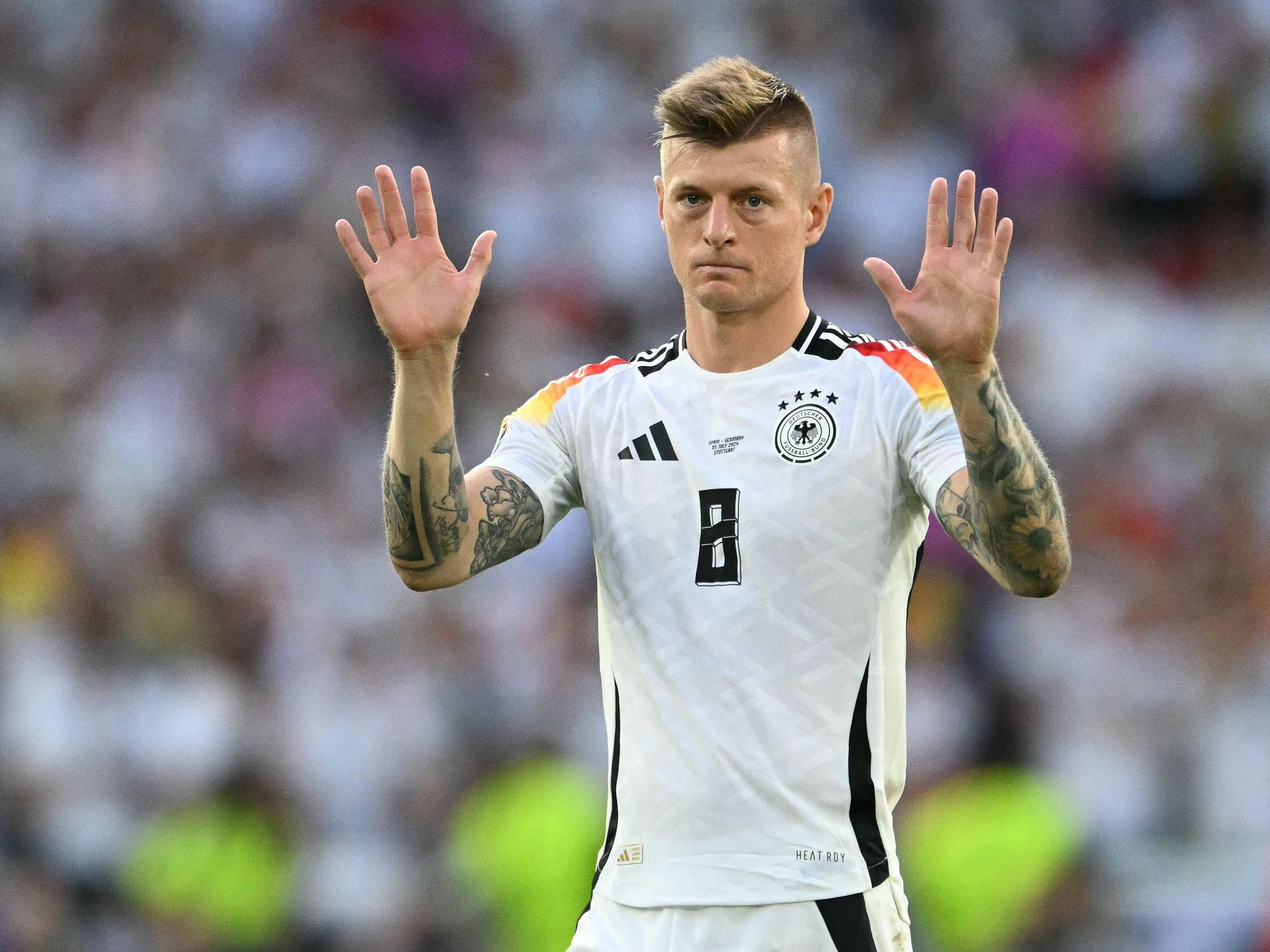 Toni Kroos hebt auf dem Platz beide Arme hoch.