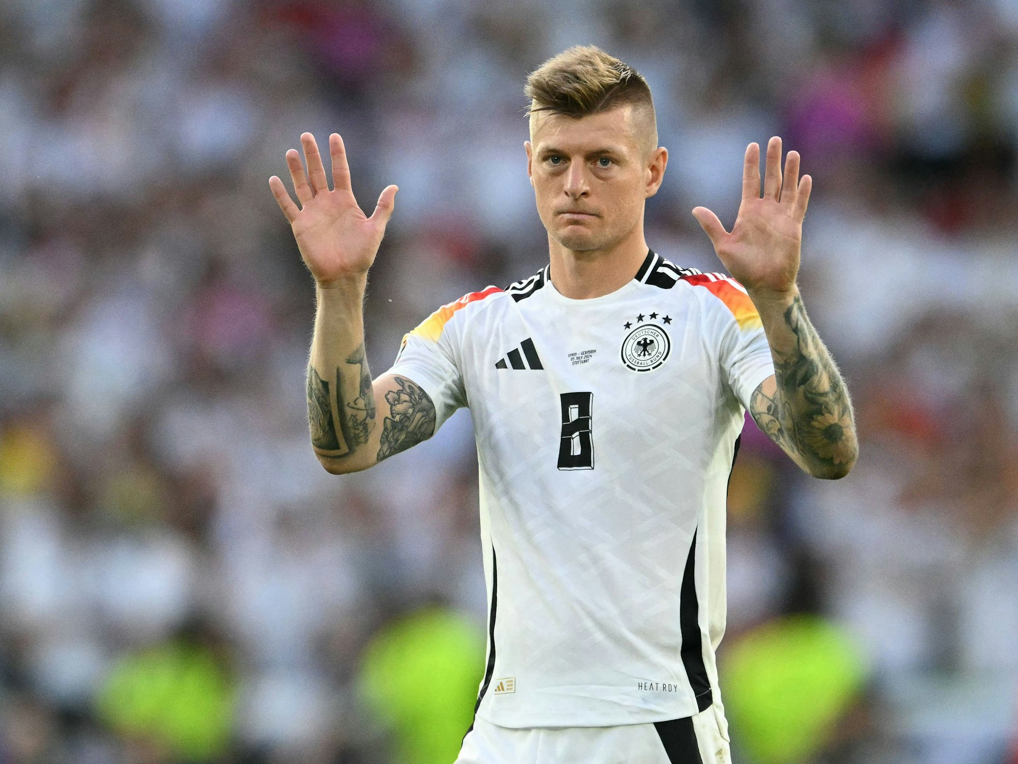Toni Kroos hebt auf dem Platz beide Arme hoch.