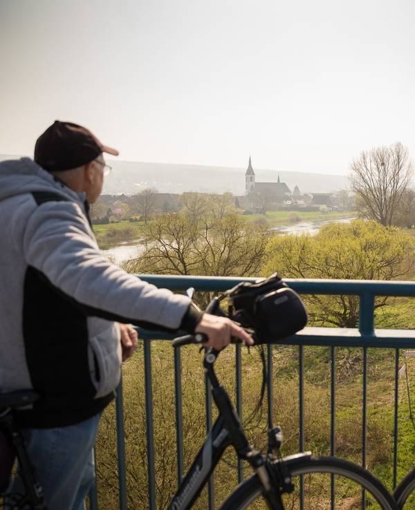Nordrhein-Westfalen, Höxter: Ein Fahrradfahrer und eine Fahrradfahrerin blicken, von einer Brücke aus, auf die Weser