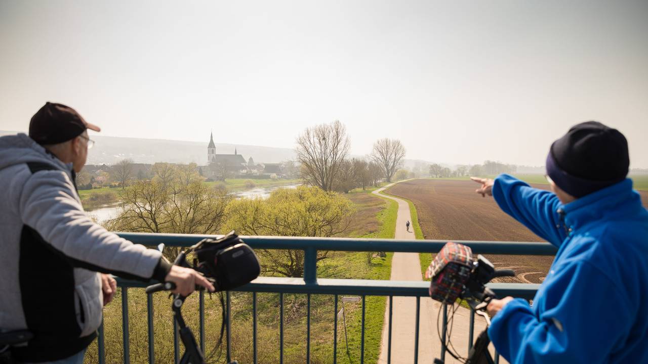 Nordrhein-Westfalen, Höxter: Ein Fahrradfahrer und eine Fahrradfahrerin blicken, von einer Brücke aus, auf die Weser