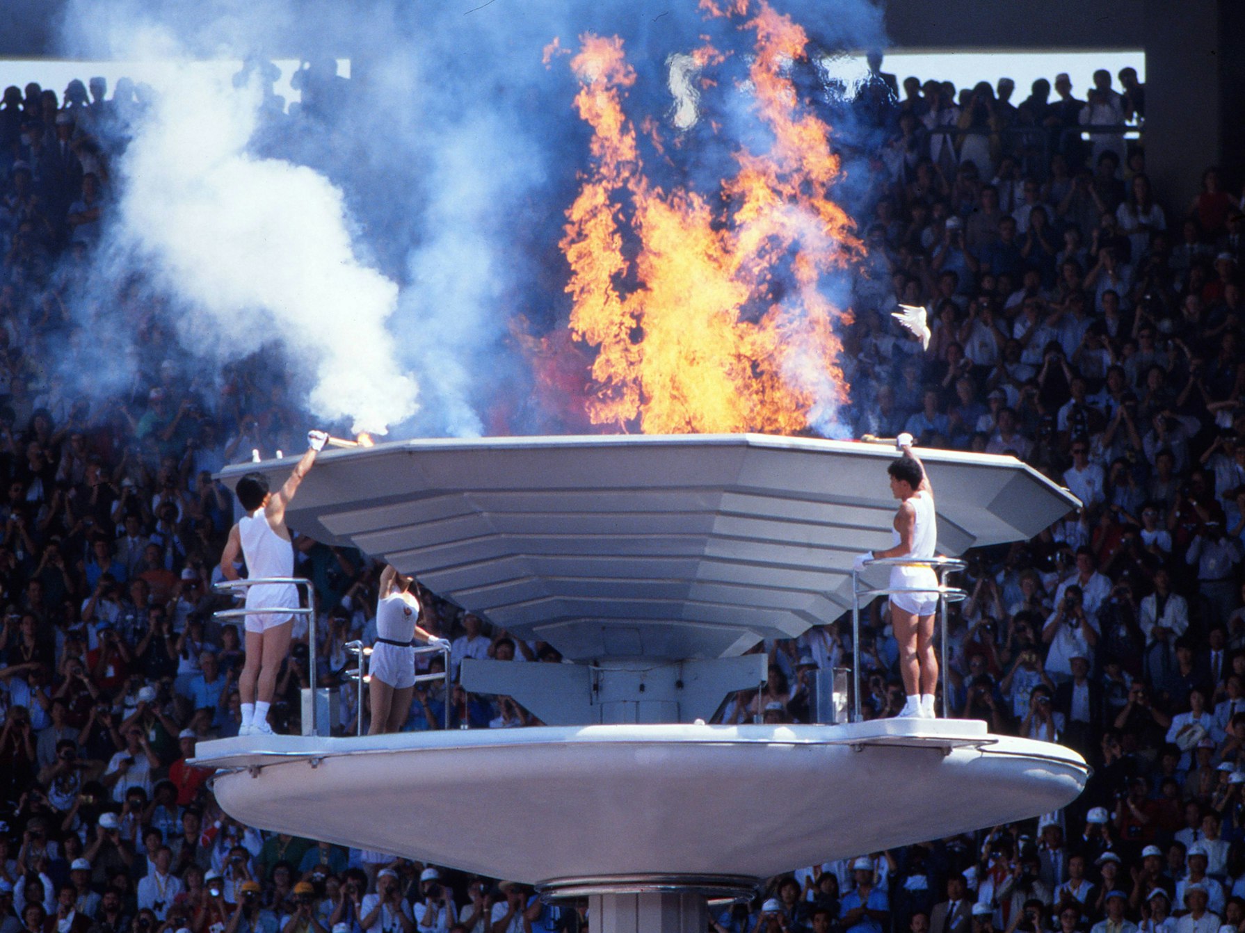Eine Taube fliegt bei der Eröffnungsfeier der Olympischen Spiele 1988 in Seoul über das olympische Feuer.