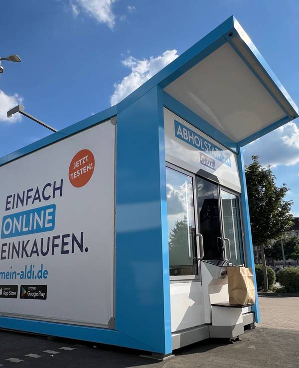 Ein Abholautomat steht an einem Parkplatz vor einer Filiale des Discounters.