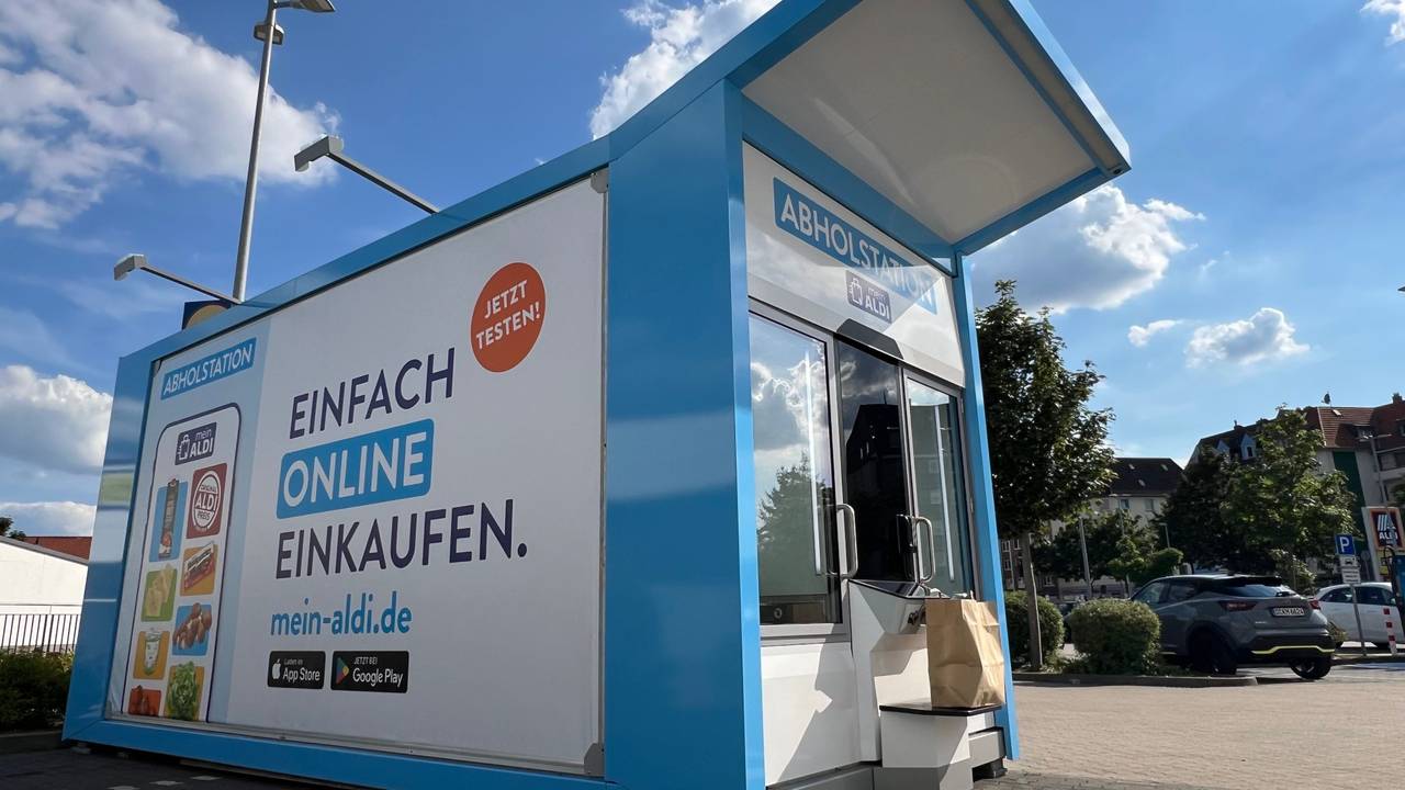 Ein Abholautomat steht an einem Parkplatz vor einer Filiale des Discounters.
