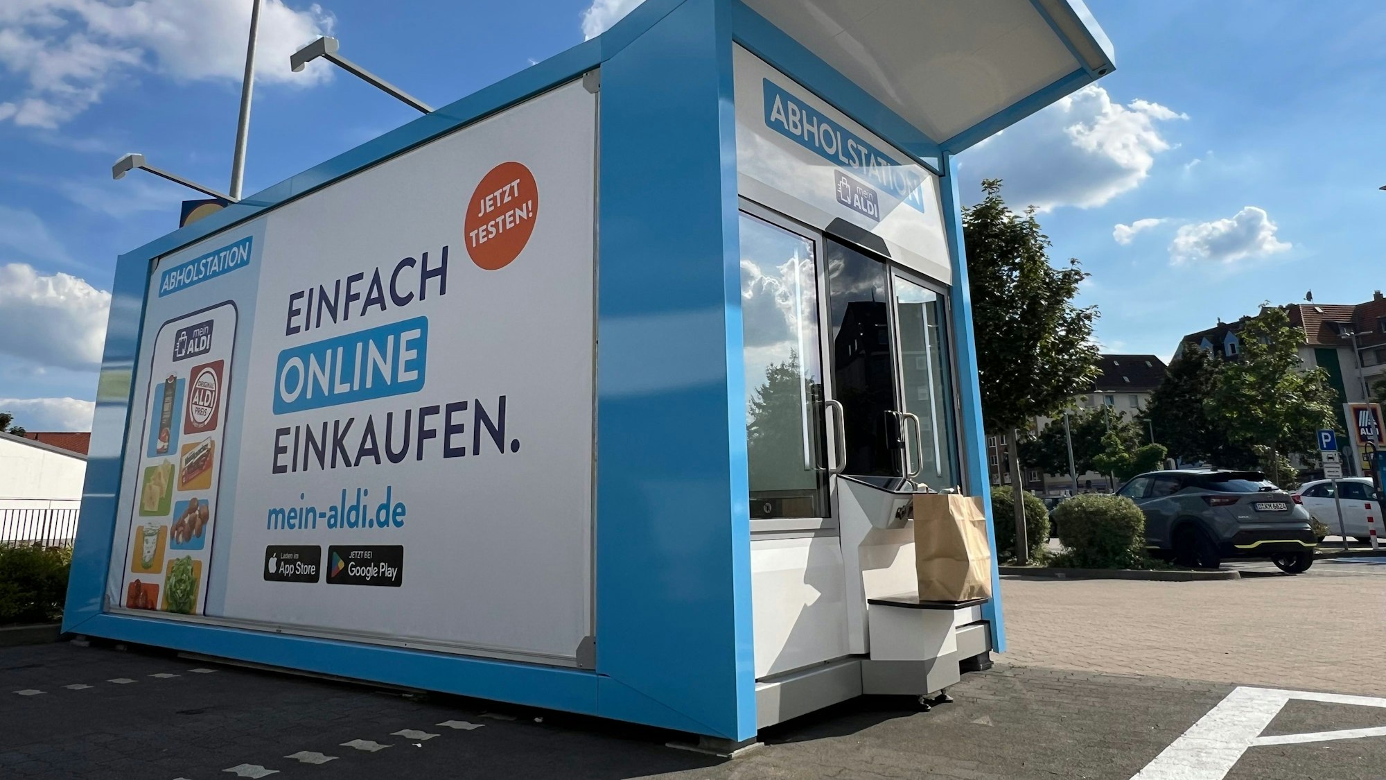 Ein Abholautomat steht an einem Parkplatz vor einer Filiale des Discounters.