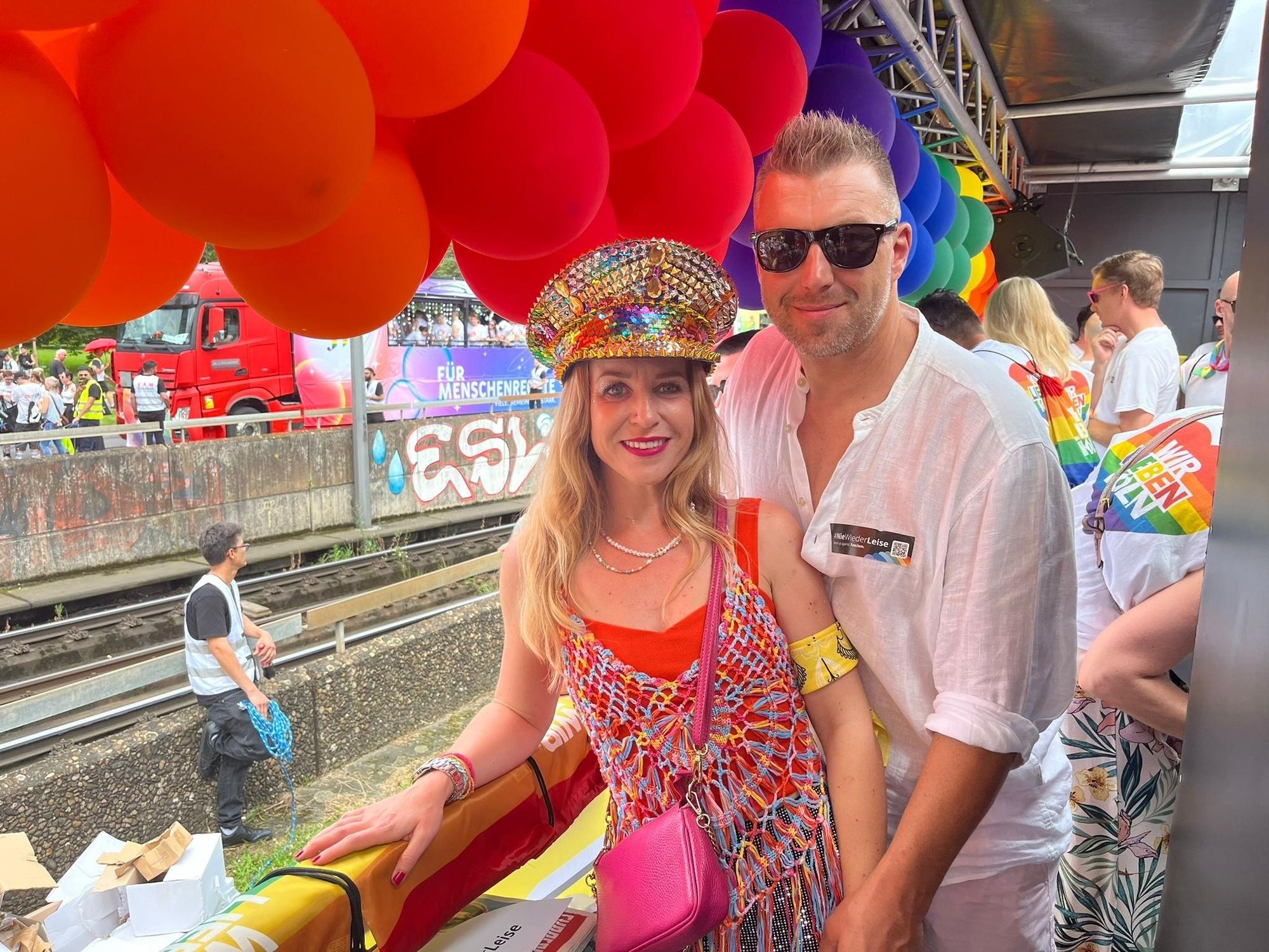 Eine Frau und ein Mann stehen auf einem Paradewagen und halten Händchen.