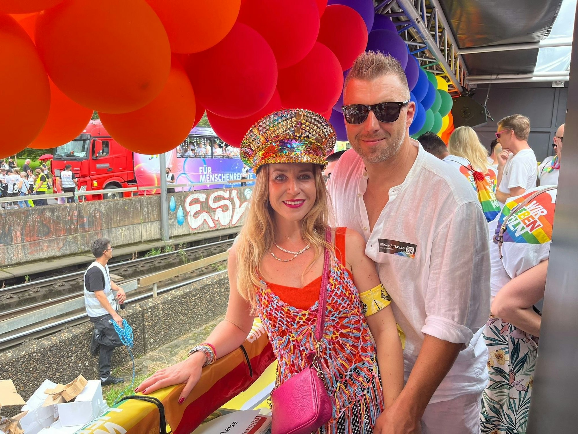 Eine Frau und ein Mann stehen auf einem Paradewagen und halten Händchen.