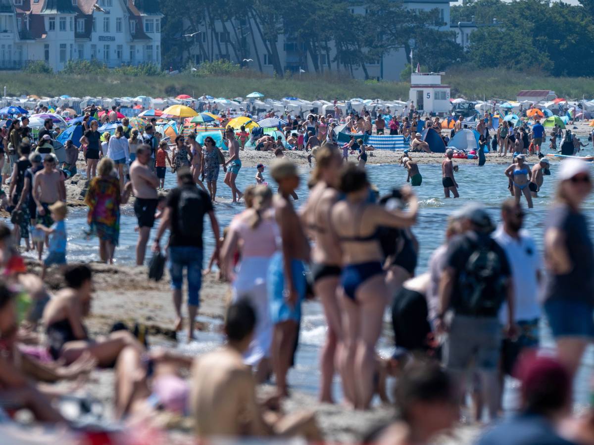 Touristen und Touristinnen spazieren und baden am Strand der Ostsee in Warnemünde.
