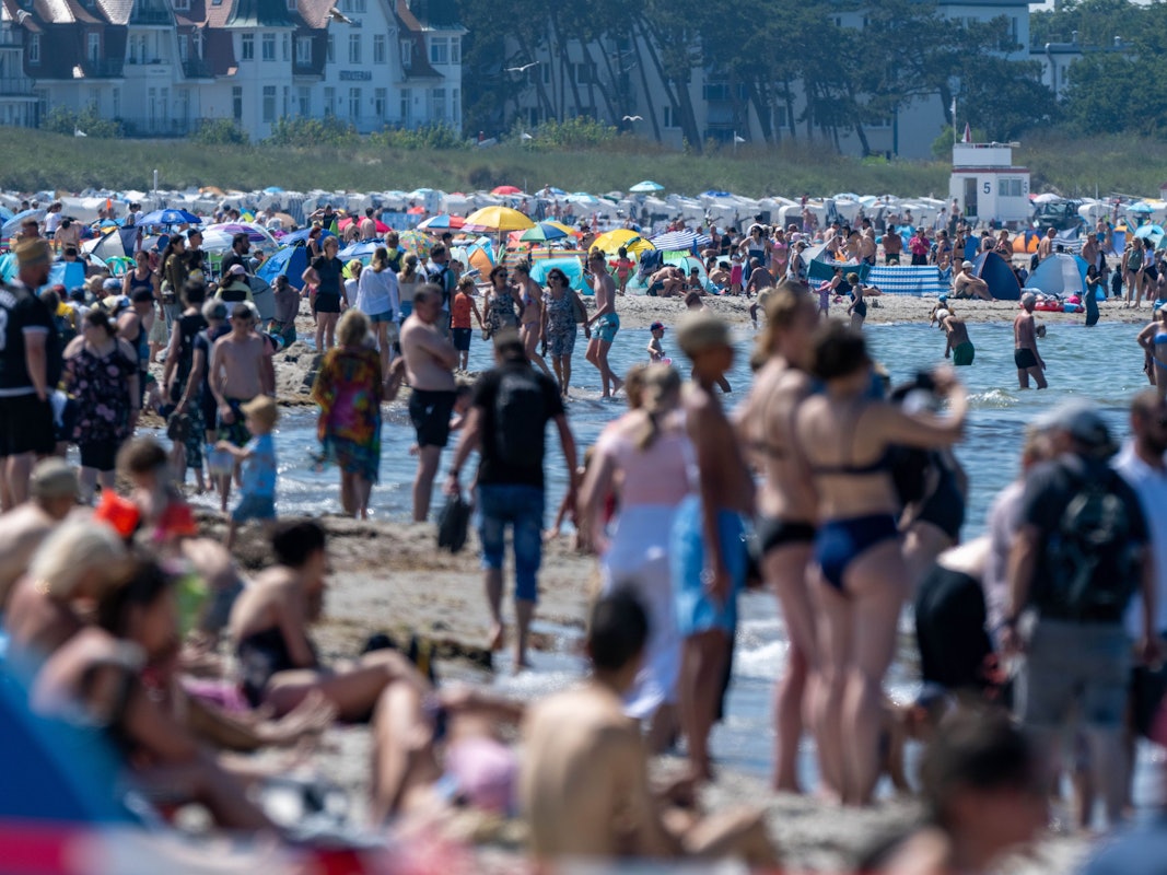 Touristen und Touristinnen spazieren und baden am Strand der Ostsee in Warnemünde.