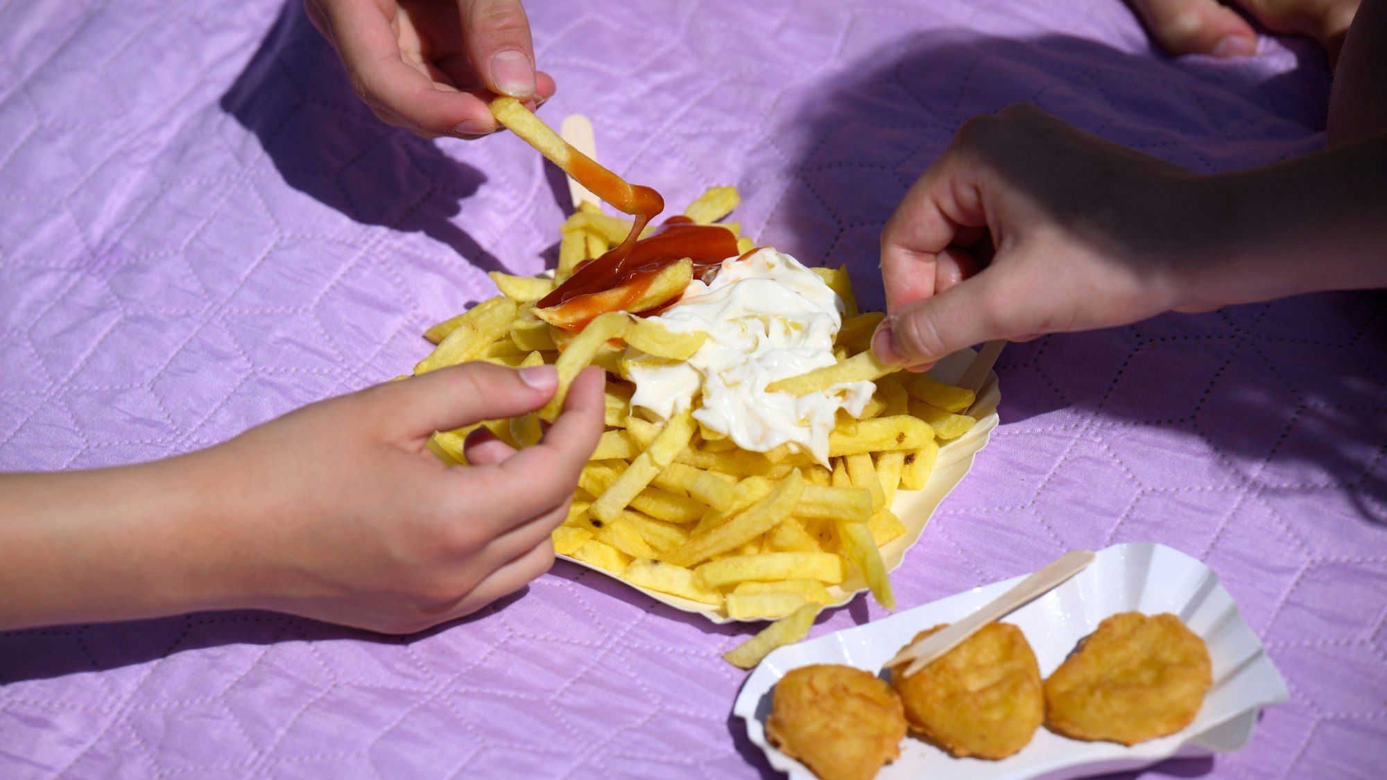 Drei Freibad-Gäste teilen sich eine Pommes.