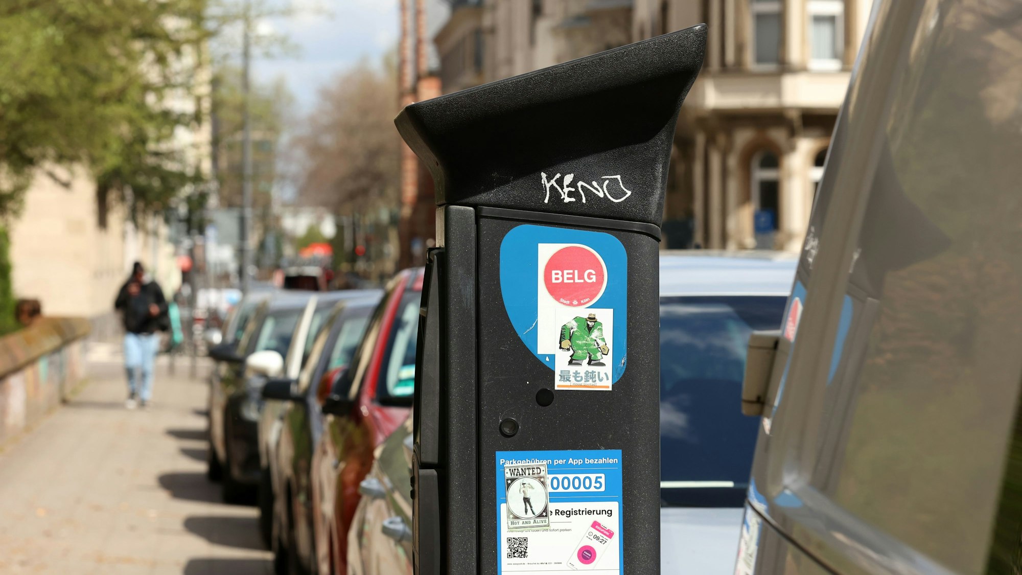 Ein Parkscheinautomat steht in Köln vor einer Reihe von Fahrzeugen.