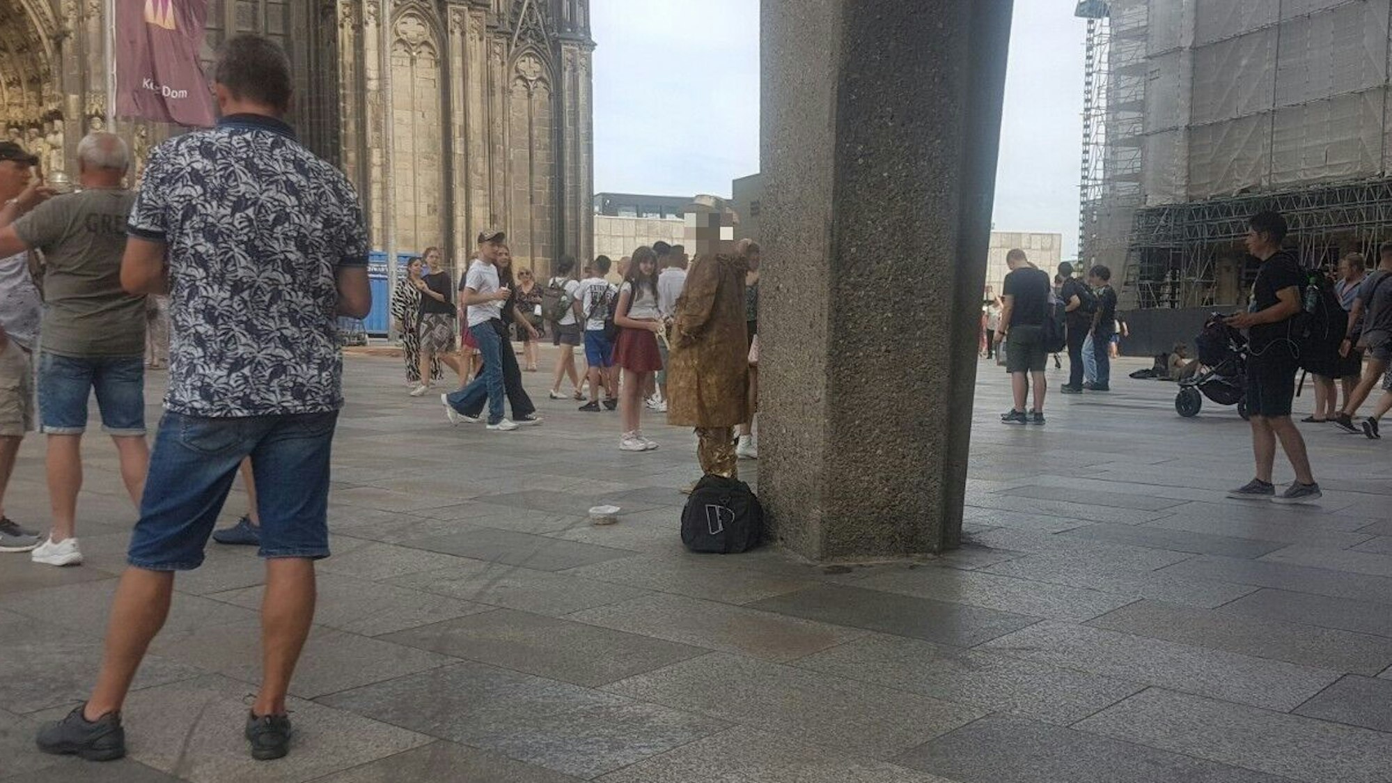 Ein Straßenkünstler, der als goldfarbener Cowboy verkleidet ist, steht am Dom.