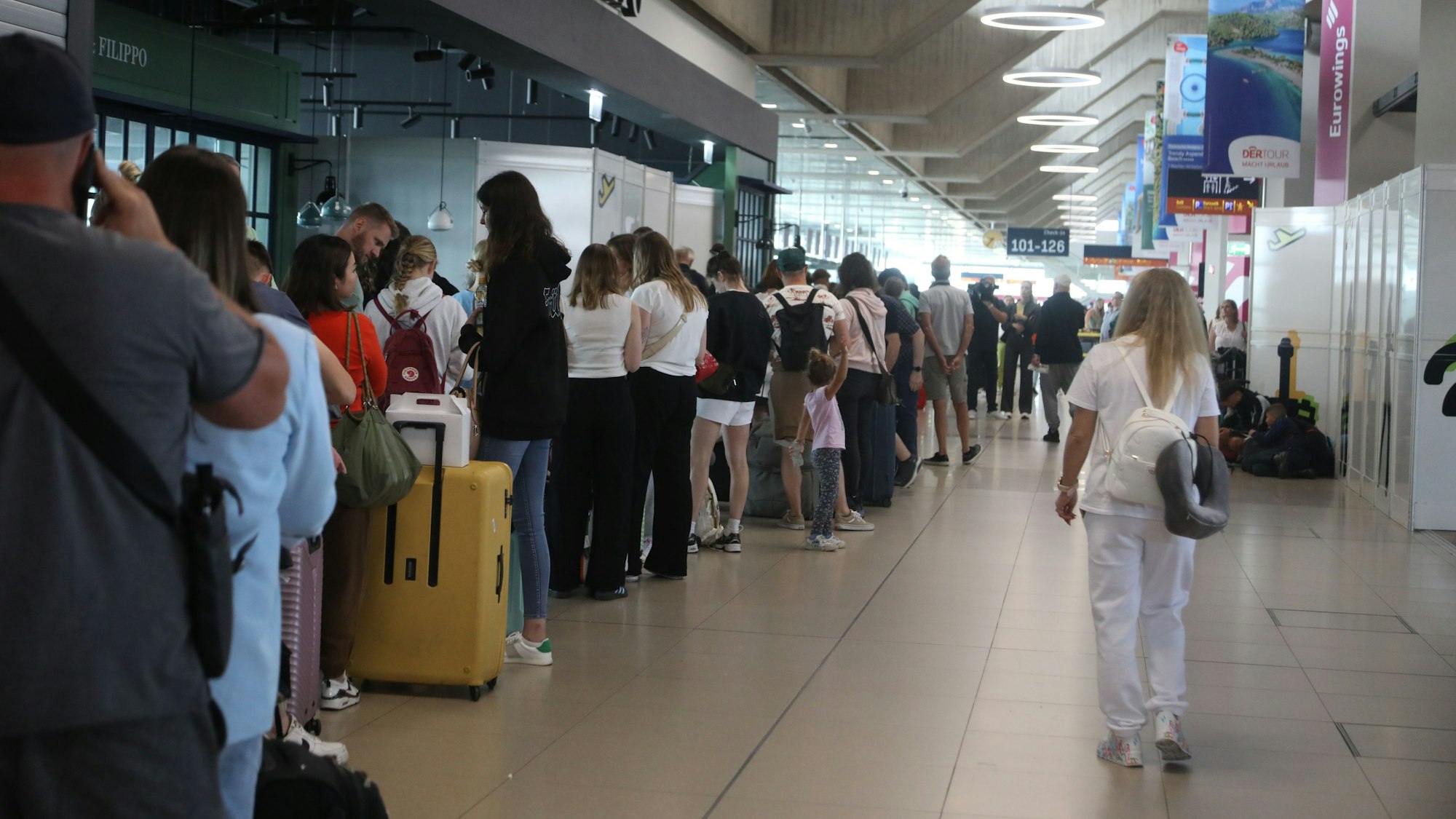Menschen warten am Flughafen Köln/Bonn in einer Schlange auf ihren Flug in den Urlaub.