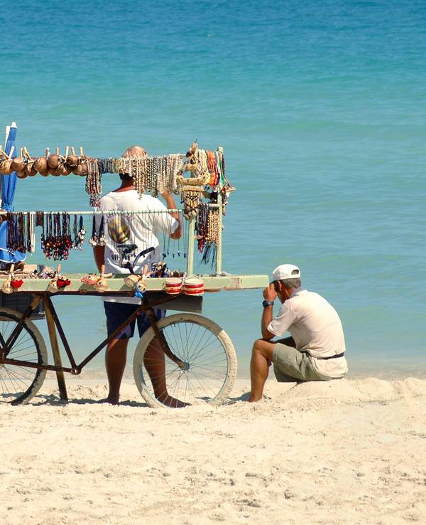 Ein Mann mit Fahrrad verkauft Gegenstände am Strand.