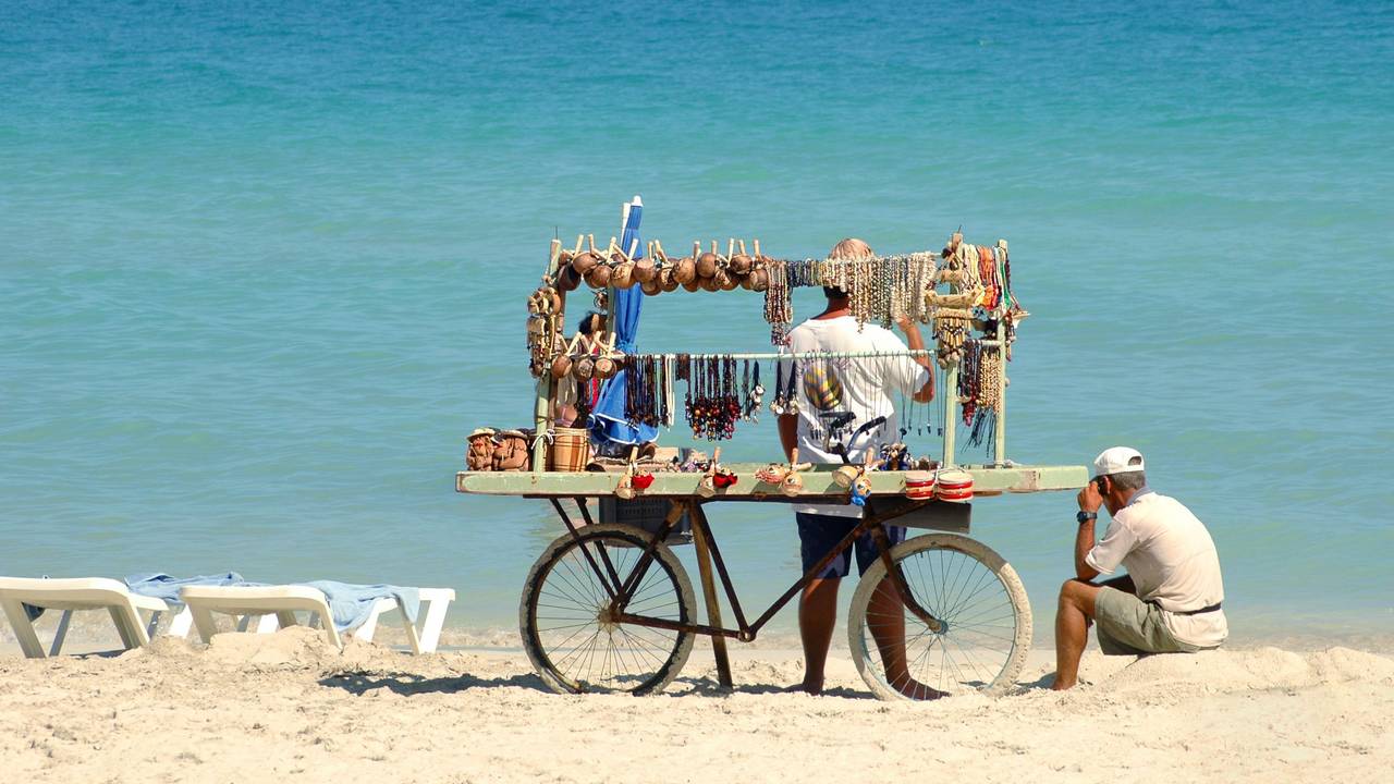Ein Mann mit Fahrrad verkauft Gegenstände am Strand.