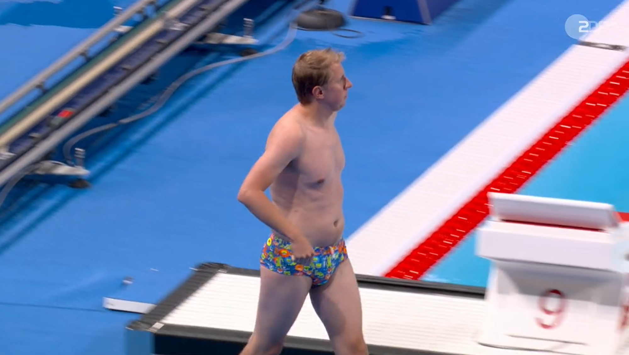 Ein Mann in bunter Badehose kommt zum olympischen Becken in Paris.