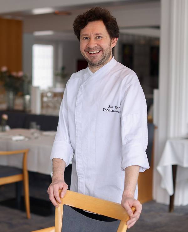 Koch Thomas Lösche steht an einem Stuhl in seinem Restaurant