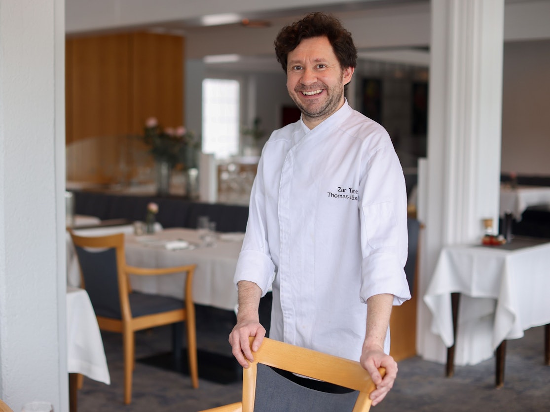 Koch Thomas Lösche steht an einem Stuhl in seinem Restaurant