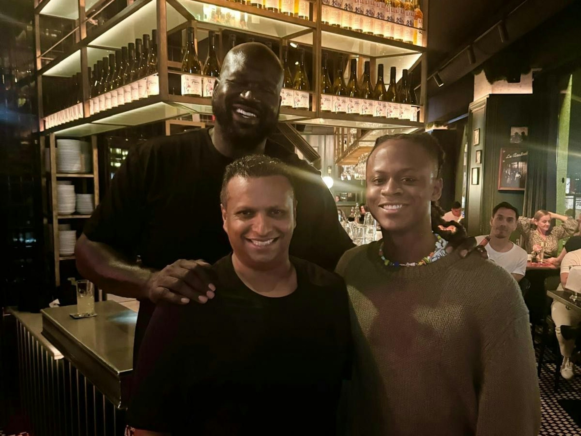 Shaquille O'Neal steht mit zwei Männern in einem Café.