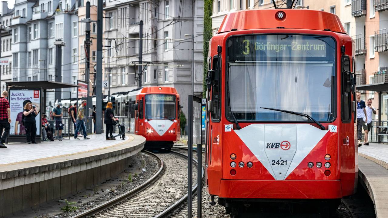 Zwei KVB-Bahnen fahren an einer Haltestelle vorbei.