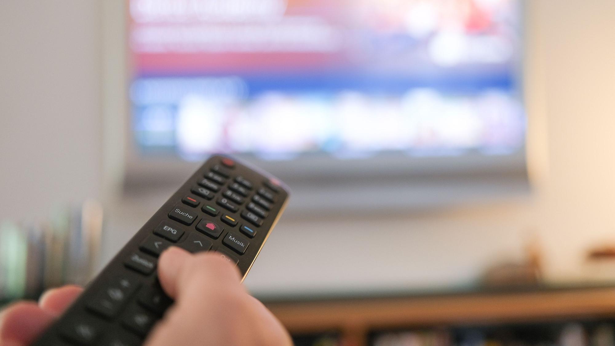 Eine Hand bedient eine Fernbedienung für ein TV-Gerät.