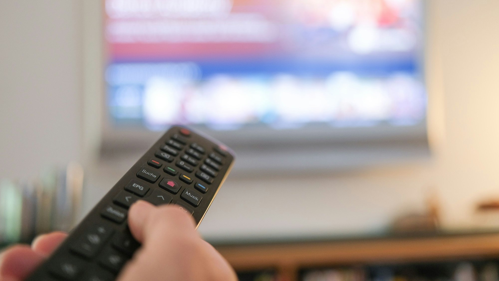 Eine Hand bedient eine Fernbedienung für ein TV-Gerät.