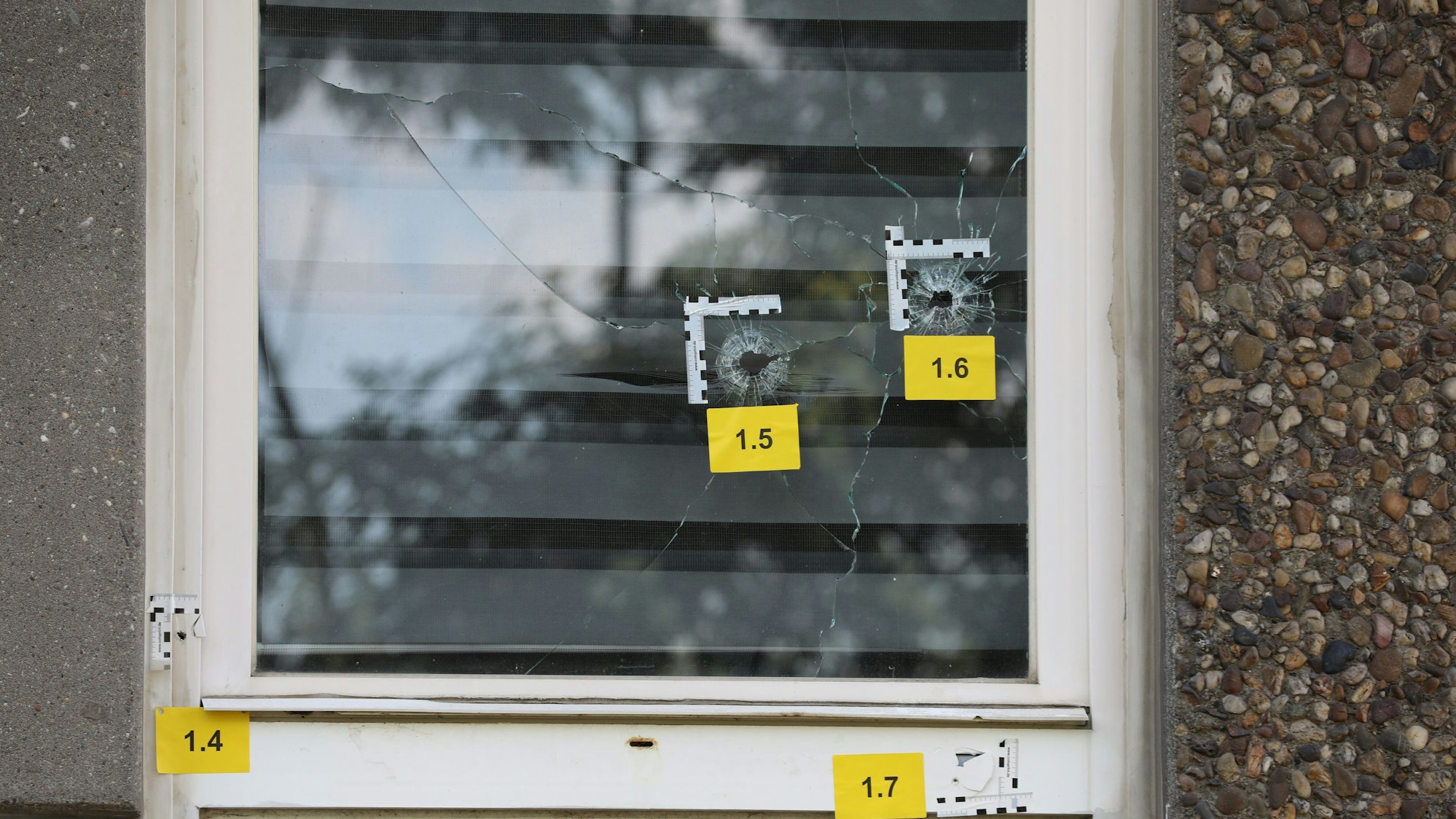 Einschusslöcher sind an einem Fenster im Erdgeschoss eines Gebäudes zu sehen.